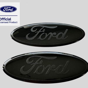 May include: Two oval-shaped black Ford emblems with a glossy finish and matte black script lettering. The Ford logo is centred on each piece. A white square in the top left corner displays the blue Ford logo and the text Official Licensed Product.