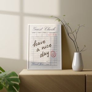 May include: White framed print with a black and white image of a restaurant check with the text "Guest Check" and "have a nice day" with a smiley face drawn in red.