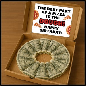 May include: A cardboard pizza box containing a circular arrangement of rolled-up £100 notes. The box lid features a sign saying "THE BEST PART OF A PIZZA IS THE DOUGH! HAPPY BIRTHDAY!" with pizza slice illustrations.