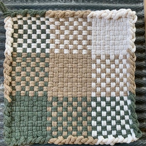 May include: A woven kitchen pot holder with a checkered pattern in green, beige, and white. The pot holder has a braided border.