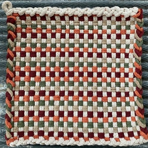 May include: A woven kitchen mat with a checkered pattern in shades of brown, orange, and red. The mat has a braided border.