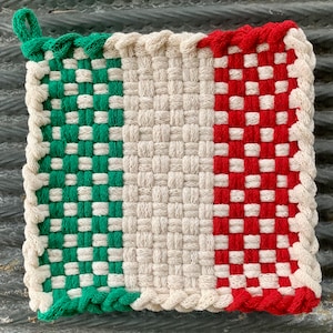 May include: A square, woven hot pad with a loop for hanging. The pad features a color block design with green, white, and red vertical stripes, and a braided white border. The woven pattern is visible throughout the design.