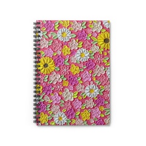 May include: A spiral-bound notebook with a vibrant floral design. The cover features a textured pattern of colorful flowers in shades of pink, yellow, white, and green against a pink background. The notebook's spiral binding is black.