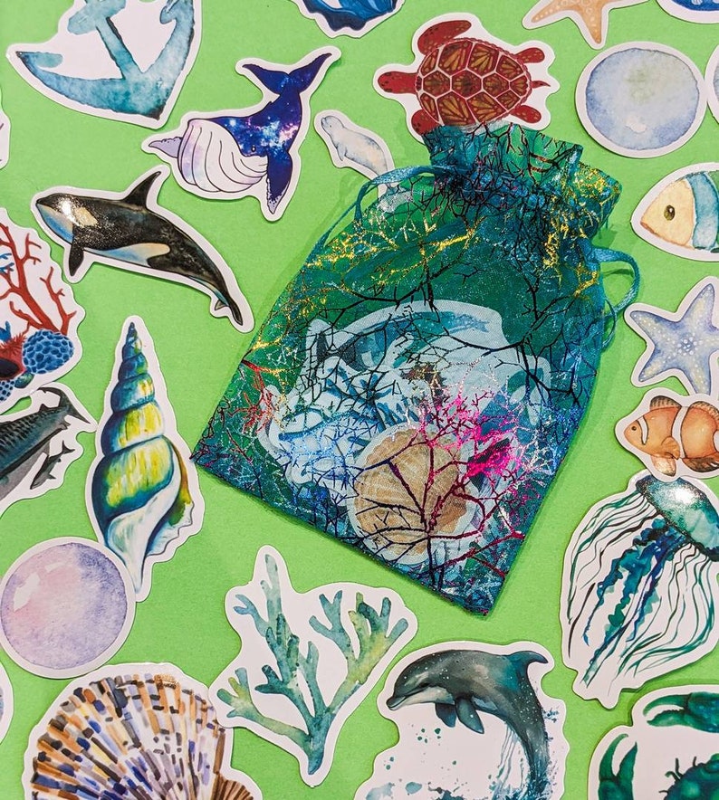 Peut inclure: Une collection d'autocollants color&eacute;s sur le th&egrave;me de l'oc&eacute;an repr&eacute;sentant une vari&eacute;t&eacute; de cr&eacute;atures marines, notamment une baleine, une tortue, une m&eacute;duse, une &eacute;toile de mer, un coquillage et un r&eacute;cif corallien. Les autocollants sont dispos&eacute;s sur un fond vert.