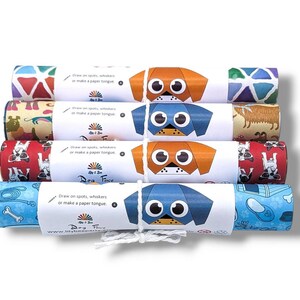 Pode incluir: Cinco rolos de papel de embrulho coloridos com rostos de c&atilde;es e padr&otilde;es. Cada rolo tem um r&oacute;tulo branco com o texto "Desenhe manchas, bigodes ou fa&ccedil;a uma l&iacute;ngua de papel." e o logotipo "Dog Face by J & J".