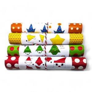 May include: Four rolls of patterned paper tied together with red, white, and green string. Each roll features a white centre band with printed origami instructions and illustrations of party hats, stars, Christmas trees, and a Santa Claus face.