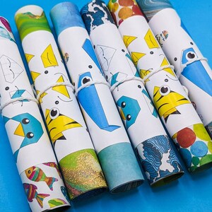 Peut inclure: Un ensemble de huit instructions d'origami en papier enroul&eacute;es, avec des motifs et des illustrations de poissons color&eacute;s. Les instructions sont attach&eacute;es avec une ficelle blanche et ont un fond bleu.