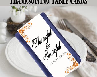 Könnte beinhalten: Tischkarten für Thanksgiving mit den Worten "Thankful & Grateful" in eleganter Schrift. Die Karten sind weiß mit orangefarbenen floralen Akzenten und einem marineblauen Rand. Der Text "Ready To Print" steht unten.
