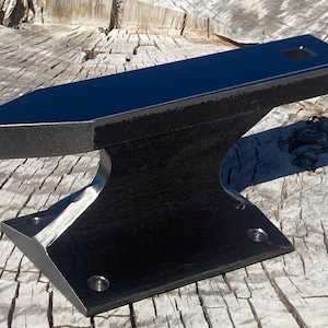 May include: A black metal anvil with a polished top and a textured base. The anvil has a rectangular work surface with a square hole and a pointed horn. The base has a flat surface with three holes.