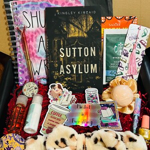 Pode incluir: Uma caixa de presente cheia de vários itens, incluindo um livro intitulado "Sutton Asylum", um caderno, adesivos, uma bomba de banho, chocolate quente Starbucks e outros acessórios. A caixa contém uma variedade de cores e texturas.