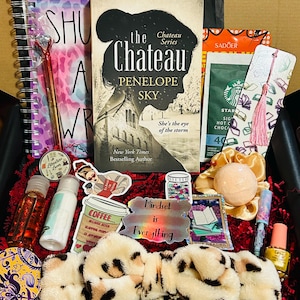 Pode incluir: Uma caixa de presente cheia de vários itens, incluindo um livro intitulado "The Chateau Series" de Penelope Sky, um caderno espiral, uma caneta, adesivos, produtos de banho e uma faixa de cabelo com estampa de leopardo. A caixa contém o texto "Mindset is Everything".