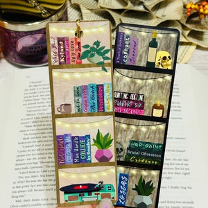 Peut inclure: Deux marque-pages en bois avec un design de bibliothèque. Le marque-page de gauche présente un tourne-disque et une plante. Le marque-page de droite présente un crâne et une bouteille de vin. Les deux marque-pages ont des lumières de fée et les titres des livres sur les étagères.