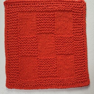 May include: A square, hand-knitted washcloth in a vibrant orange color. The textile features a textured pattern created by alternating blocks of stockinette stitch and garter stitch, forming a grid-like design across the entire surface.