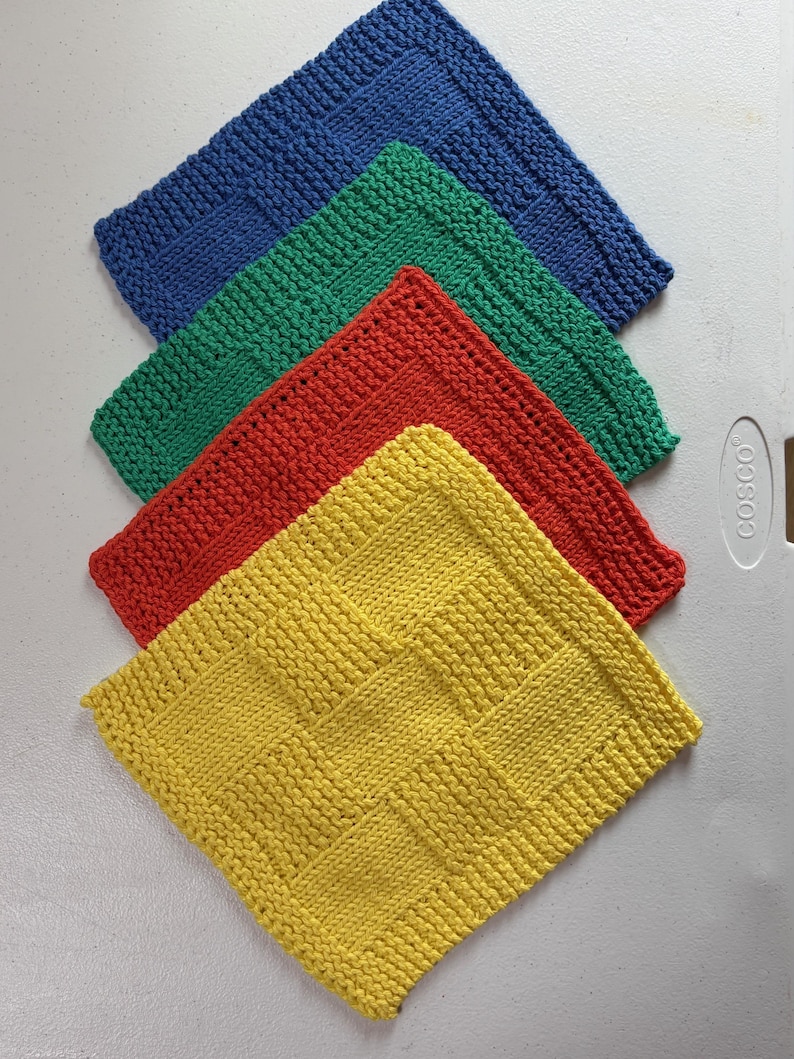 May include: A set of four square knitted dishcloths arranged in a stack. The cloths are solid blue, green, red, and yellow, each featuring a textured basketweave pattern with a garter stitch border. The items are displayed in a layered formation.