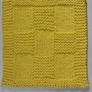 May include: A square, bright yellow knitted dishcloth featuring a textured pattern of alternating garter stitch and stockinette stitch blocks. The design consists of a central square surrounded by a border of smaller rectangular blocks in a grid.