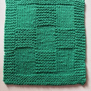May include: A square, hand-knitted washcloth in a vibrant emerald green color. The textile features a textured basketweave pattern created by alternating blocks of vertical stockinette stitches and horizontal garter stitch rows throughout.