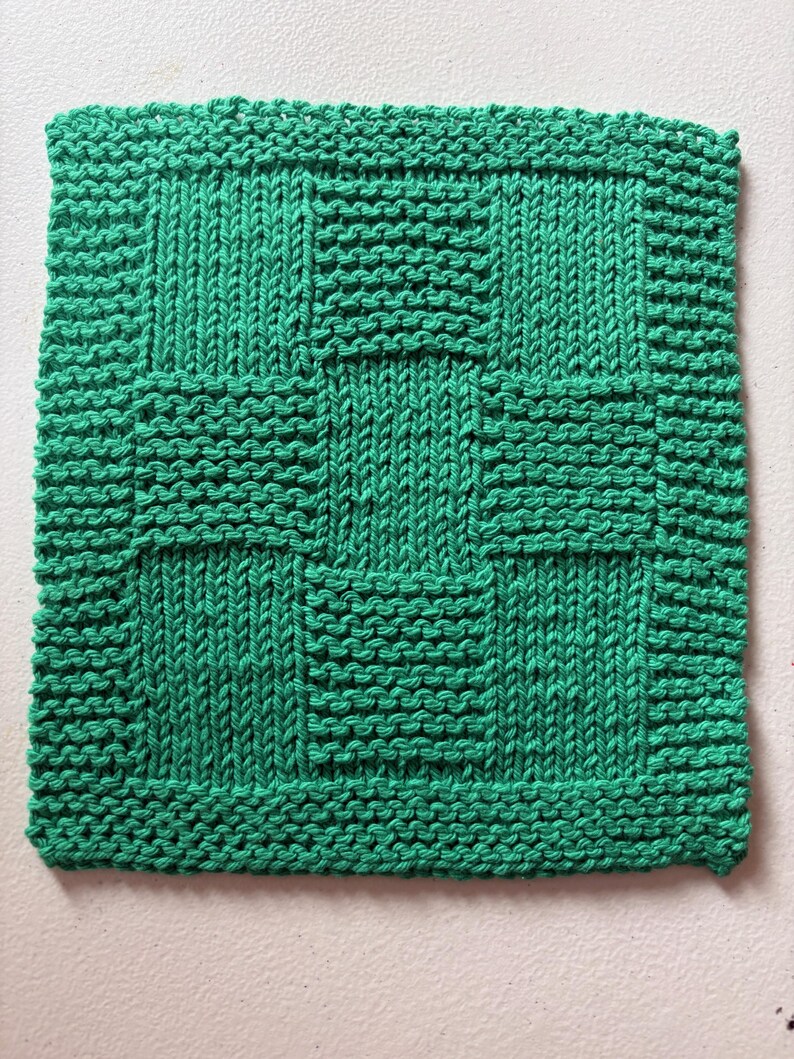 May include: A square, hand-knitted washcloth in a vibrant emerald green color. The textile features a textured basketweave pattern created by alternating blocks of vertical stockinette stitches and horizontal garter stitch rows throughout.