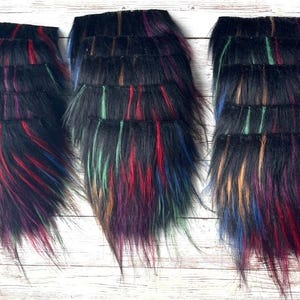 May include: Three sections of black faux fur with colorful streaks of red, green, purple, and blue. The fur is arranged in layered rows, creating a textured appearance. The background is a light-colored wooden surface.
