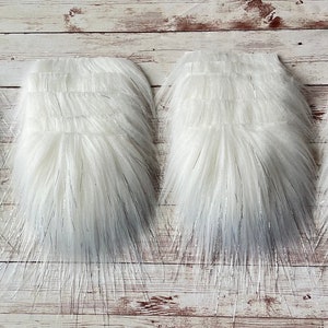 May include: Four rectangular pieces of white faux fur with long, soft fibers. The fur has a slight sheen and a subtle silver thread running through it, creating a textured appearance. The pieces are arranged side by side.