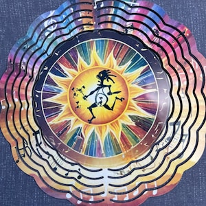 May include: A multi-layered metal wind spinner featuring a central sun design with a Kokopelli figure. The sun's rays are in vibrant colors. The outer layers have musical notes cut out, creating a decorative and musical theme.