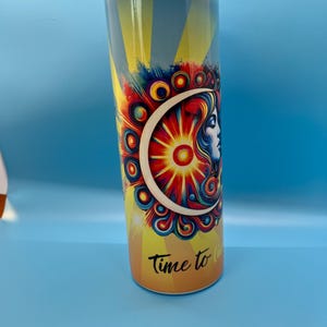 Puede incluir: Un vaso de acero inoxidable colorido con un diseño psicodélico de sol y luna. El vaso tiene una tapa transparente y el texto "Time to" está impreso en la parte inferior.