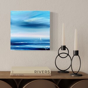 Op de afbeelding: Abstracte schilderij van een zeelandschap met twee zeilboten in de verte. Het schilderij is in tinten blauw en wit, met een vleugje roze in de lucht. Het schilderij is ingelijst en hangt aan een muur.