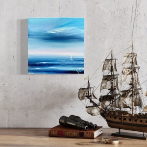 Op de afbeelding: Een blauw en wit abstract schilderij van een zeelandschap met twee zeilboten in de verte. Het schilderij is ingelijst en hangt aan een muur met een scheepsmodel, een verrekijker en een boek op de voorgrond.