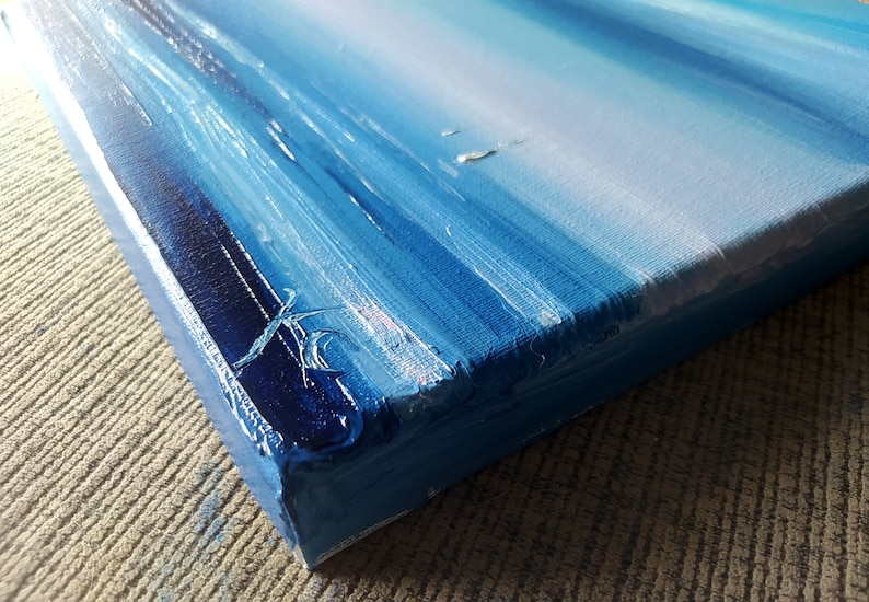 Op de afbeelding: Close-up van de zijkant van een blauw en wit abstract schilderij op canvas. Het schilderij heeft een textuur en is geschilderd met dikke penseelstreken.