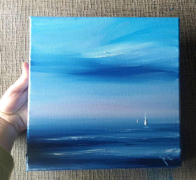 Op de afbeelding: Een schilderij van een zeezicht met een blauwe lucht en een lichtblauwe zee. Twee witte zeilboten zijn in de verte te zien.