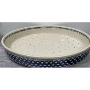 May include: A ceramic serving dish with a cream-colored interior and a blue and white patterned exterior. The rim features a scalloped design in blue and green. The interior has small, evenly spaced black dots.