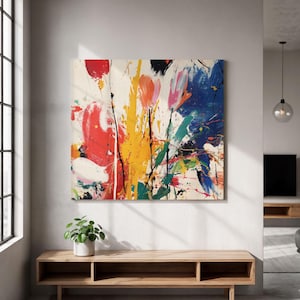 May include: Abstract art canvas with a vibrant mix of colours. The artwork features bold strokes of red, yellow, blue, and black paint, creating a dynamic and energetic composition. The canvas is displayed on a white wall above a wooden console.