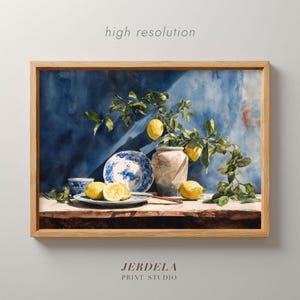 Puede incluir: Una impresión enmarcada que presenta un bodegón con limones, un plato azul y blanco y un jarrón. La obra de arte tiene un estilo de acuarela con un fondo azul y el texto "high resolution" y "JERDELA PRINT STUDIO".
