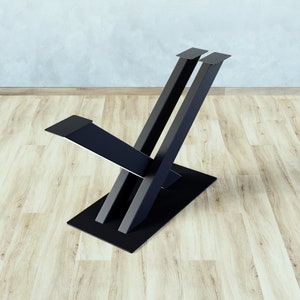 Könnte beinhalten: Ein moderner Stuhlfuß aus schwarzem Metall mit X-förmigem Design. Der Fuß hat einen rechteckigen Fuß und zwei vertikale Stützen, die nach oben abgewinkelt sind. Ein horizontales Stück erstreckt sich von den Stützen und bildet einen Sitz.