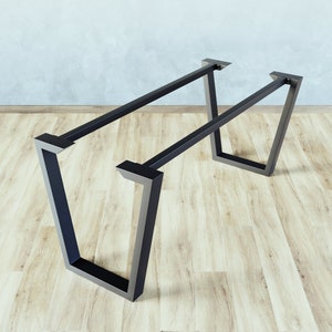 Könnte beinhalten: Schwarze Tischbeine aus Metall mit rechteckiger Form und leicht abgewinkeltem Design. Die Beine sind aus robustem Metall gefertigt und haben eine schwarze Oberfläche.