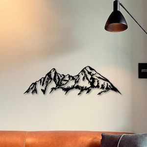 Könnte beinhalten: Schwarze Wandkunst aus Metall, die eine Silhouette einer Bergkette darstellt. Die Berge sind stilisiert und haben ein gezacktes, strukturiertes Aussehen.