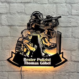 Könnte beinhalten: Eine schwarze Silhouette von drei Polizisten mit einem Schild, einem Gewehr und einem Banner mit der Aufschrift "Bester Polizist Thomas Göbel".