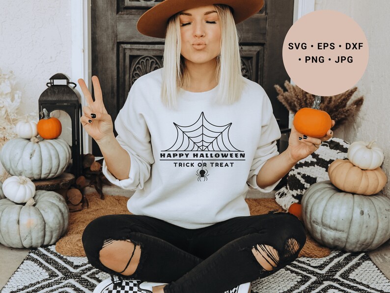 K&ouml;nnte beinhalten: Ein wei&szlig;es Sweatshirt mit einem schwarzen Spinnennetz-Design und dem Text "Happy Halloween Trick or Treat".