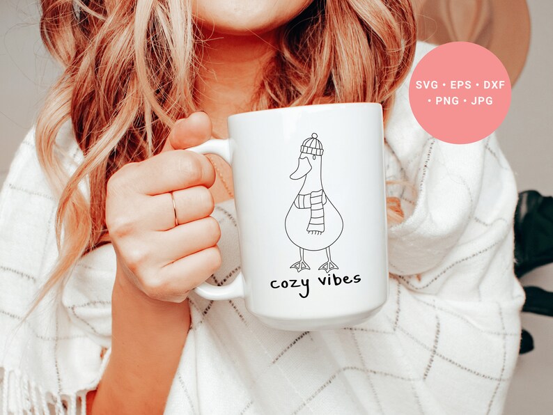 K&ouml;nnte beinhalten: Wei&szlig;e Keramiktasse mit einer schwarzen Strichzeichnung einer Gans, die einen Hut und einen Schal tr&auml;gt. Der Text "cozy vibes" ist unter der Gans aufgedruckt.