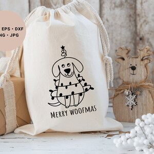 May include: A white canvas bag with a black and white illustration of a dog dressed as a Christmas tree. The text "Merry Woofmas" is printed below the illustration.