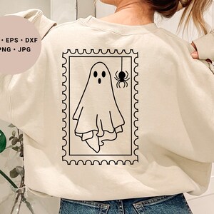 Könnte beinhalten: Beigefarbenes Sweatshirt mit einem schwarz-weißen Geister- und Spinnen-Design in einem Briefmarkenrahmen. Das Design enthält den Text "SVG • EPS • DXF • PNG • JPG" in einem Kreis.