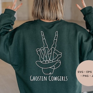 May include: A dark green sweatshirt with a white outline of a skeleton hand making a peace sign and the text "Ghostin Cowgirls".