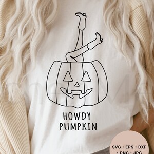 May include: A white t-shirt with a black line drawing of a person's legs sticking out of a pumpkin. The text "Howdy Pumpkin" is below the pumpkin.