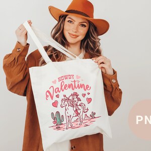 May include: White tote bag with a pink and red design featuring a cowboy riding a horse with the text "Howdy Valentine".