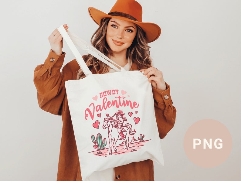 May include: White tote bag with a pink and red design featuring a cowboy riding a horse with the text "Howdy Valentine".