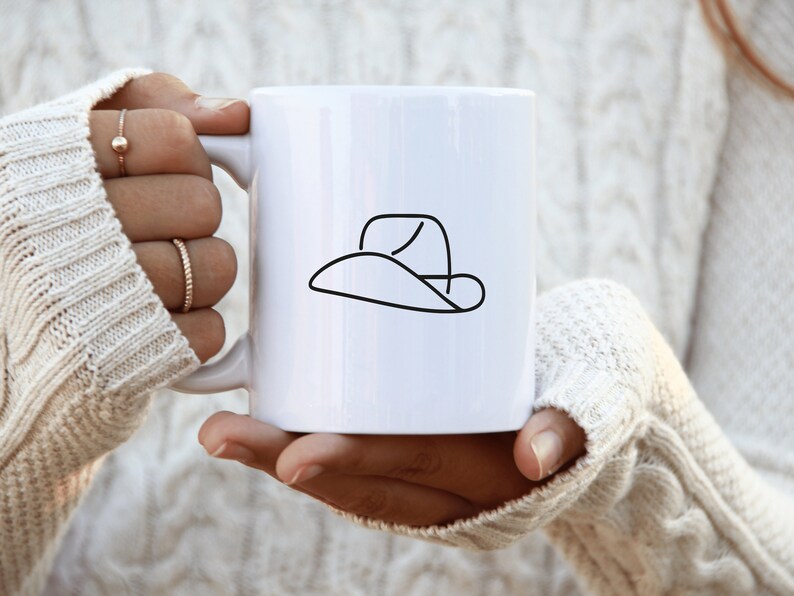 May include: White ceramic mug with a black line drawing of a cowboy hat.