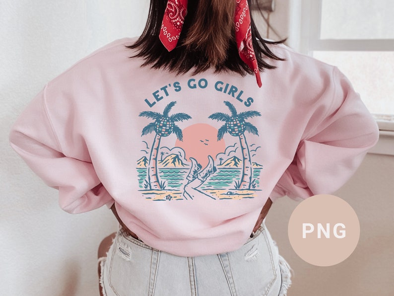 K&ouml;nnte beinhalten: Hellrosa Sweatshirt mit dem Text "LET'S GO GIRLS" &uuml;ber einer Strandszene mit Palmen, Sonnenuntergang und den Beinen einer Person in Cowboystiefeln. Das Sweatshirt hat eine hellrosa Farbe.