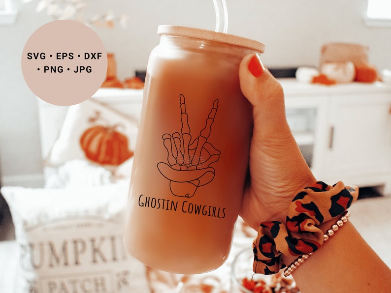 May include: A brown glass tumbler with a straw, featuring a black line drawing of a skeleton hand making a peace sign wearing a cowboy hat. The tumbler has the text "Ghostin Cowgirls" printed on it.