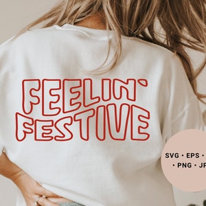 Könnte beinhalten: Weißes Sweatshirt mit rot umrandetem Text, der "Feelin' Festive" lautet. Der Text ist in einer Retro-Schriftart mit Blasen. Ein rosa Kreis in der rechten unteren Ecke des Bildes enthält den Text "SVG - EPS - DXF - PNG - JPG".