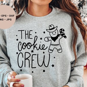 May include: A gray sweatshirt with the text "THE cookie CREW" and a gingerbread man wearing a cowboy hat and holding a candy cane.