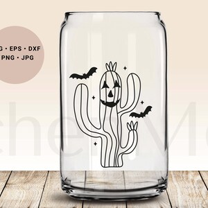 May include: A black and white illustration of a cactus with a jack-o'-lantern face and two bats flying around it. The cactus is on a clear glass can.